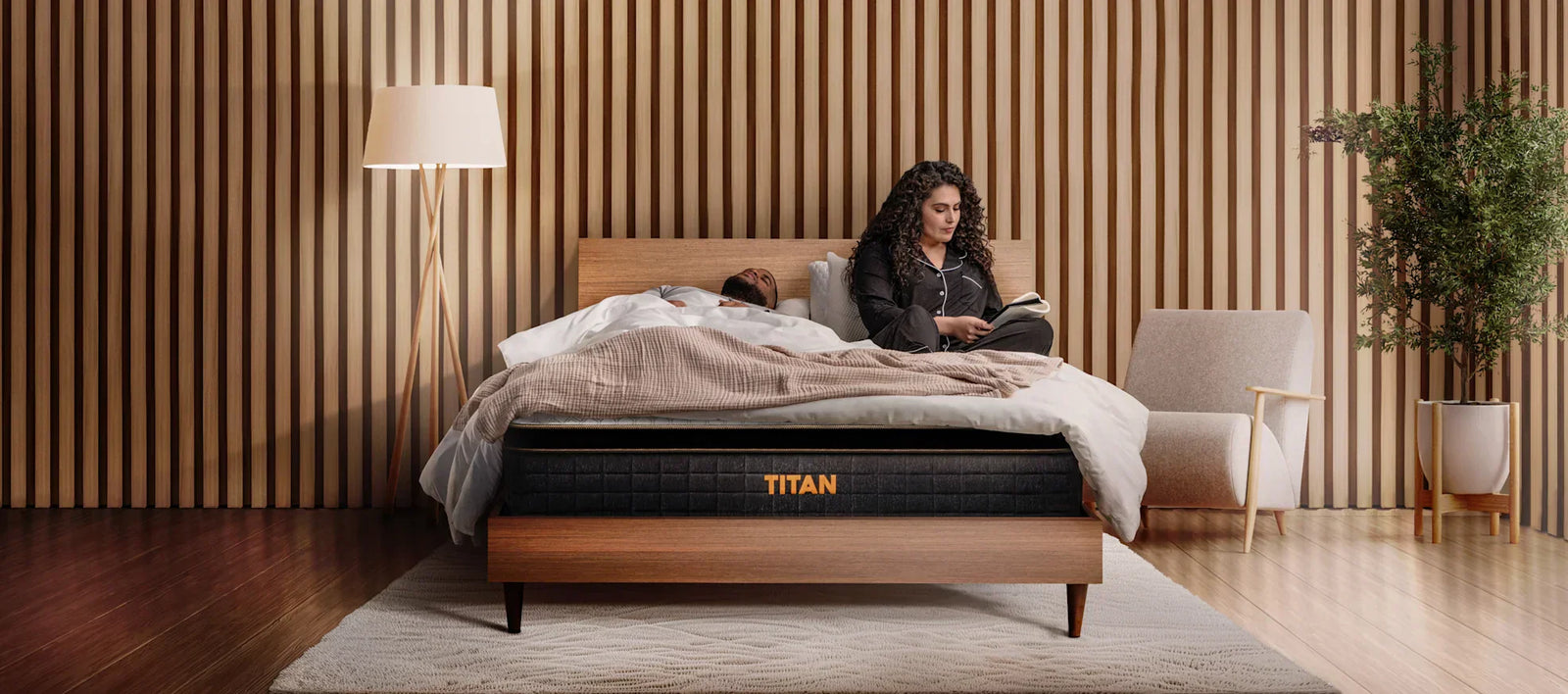 woman sitting on a Titan mattress reading a book next to a sleeping man