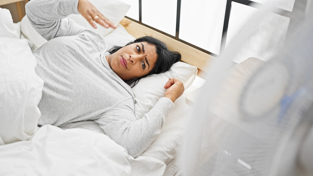 woman having hot flashes in bed, fanning herself in a white bed. 