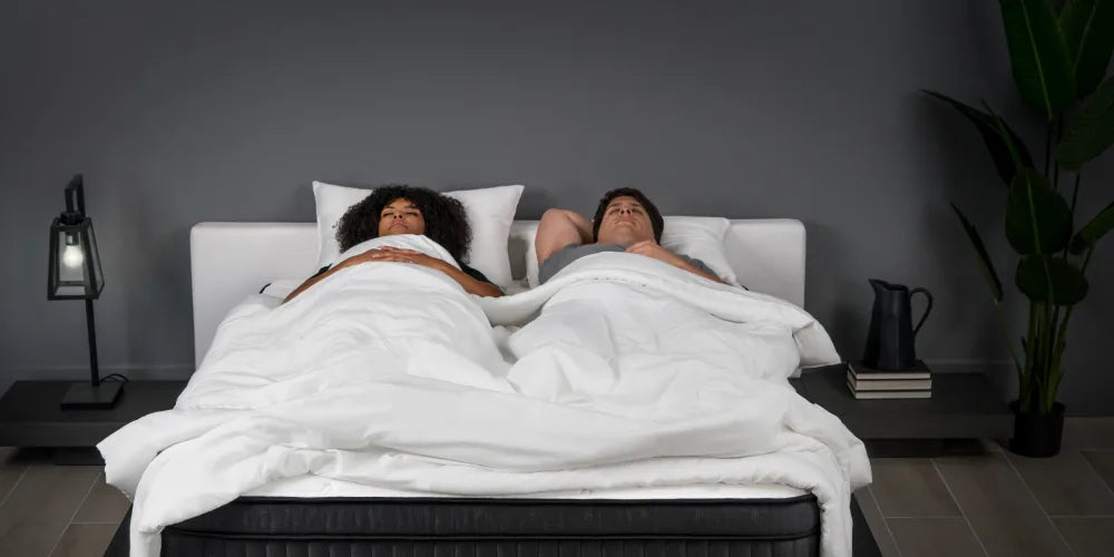 two people laying down in a white bed, set in a bedroom scene